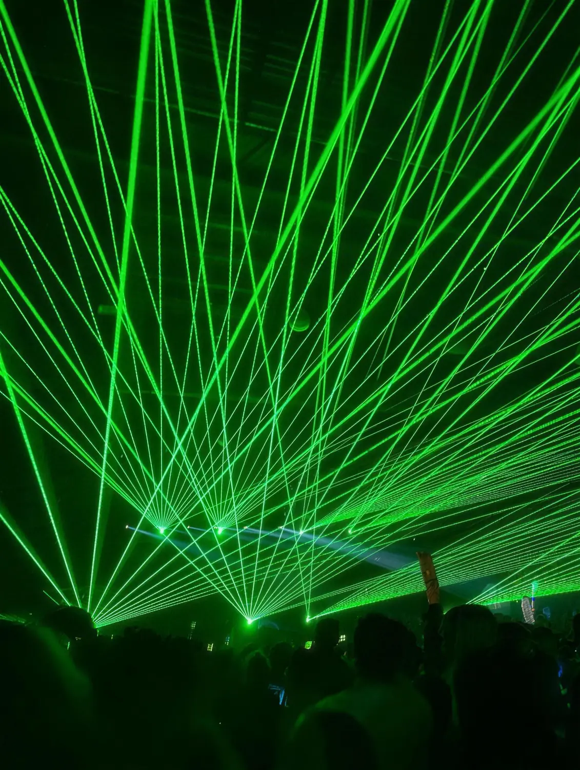 Green laser beams fanning out over a crowd at an electronic music event
